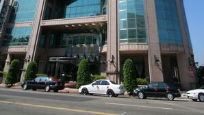 A tall, modern hotel with a curved glass facade, multiple floors, and a prominent entrance.