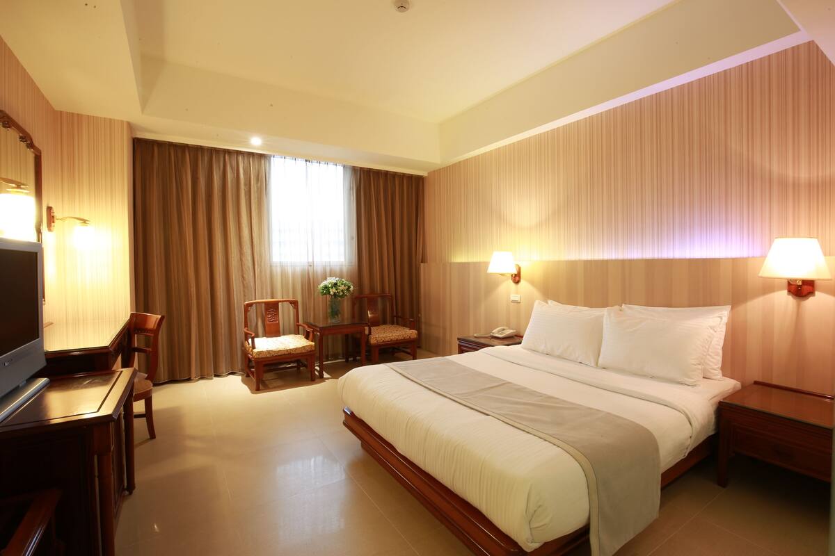 A hotel room with a large bed, a desk with a chair, a TV, and two bedside lamps.