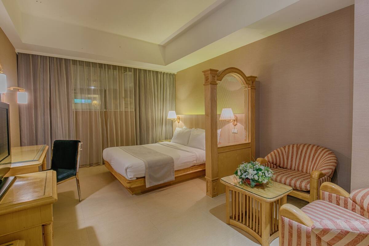 A hotel room with a bed, a desk, a chair, a sofa, a mirror, and a window with curtains.