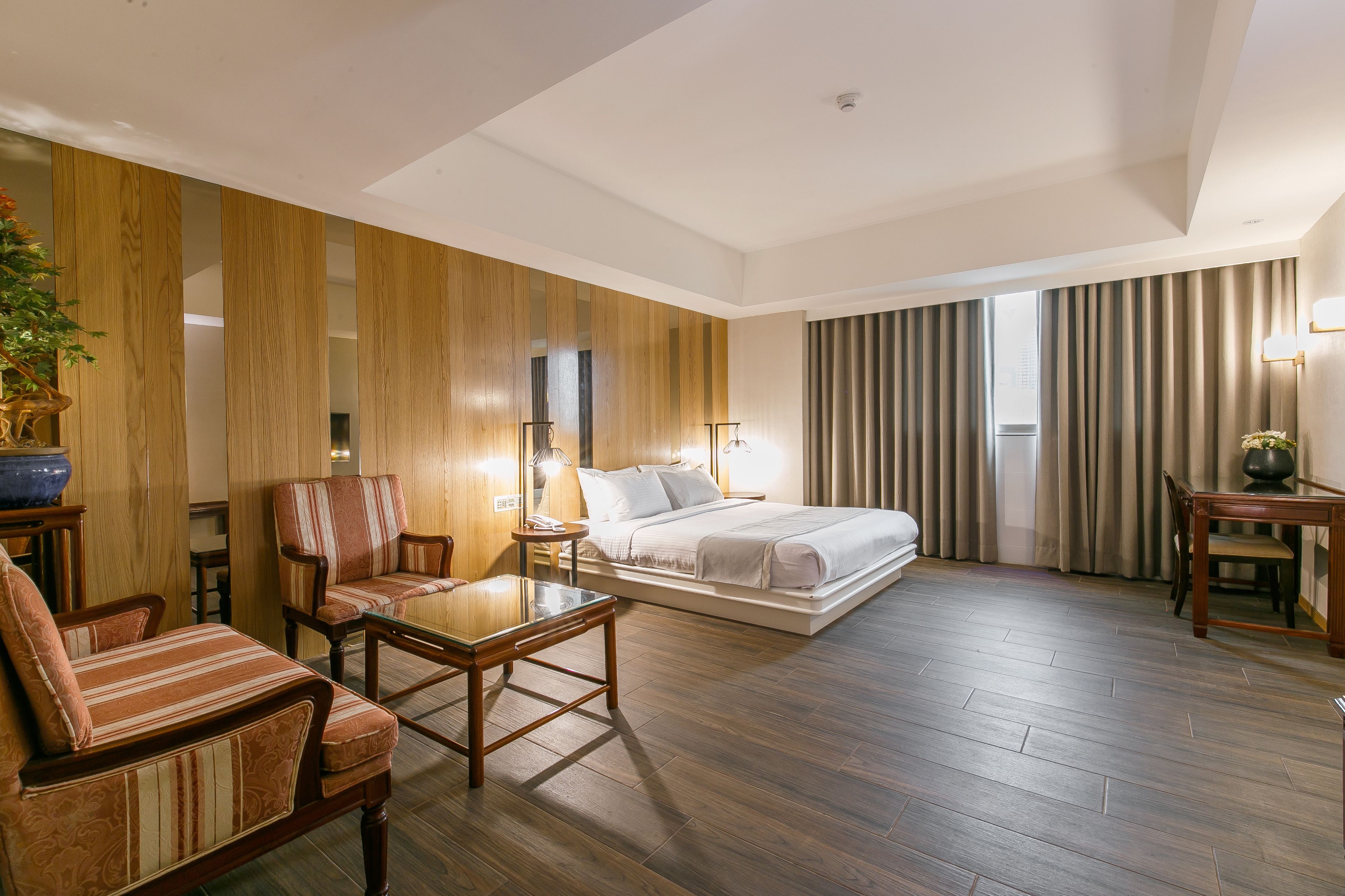 A hotel room with a bed, a seating area with a table, and a large window with curtains.