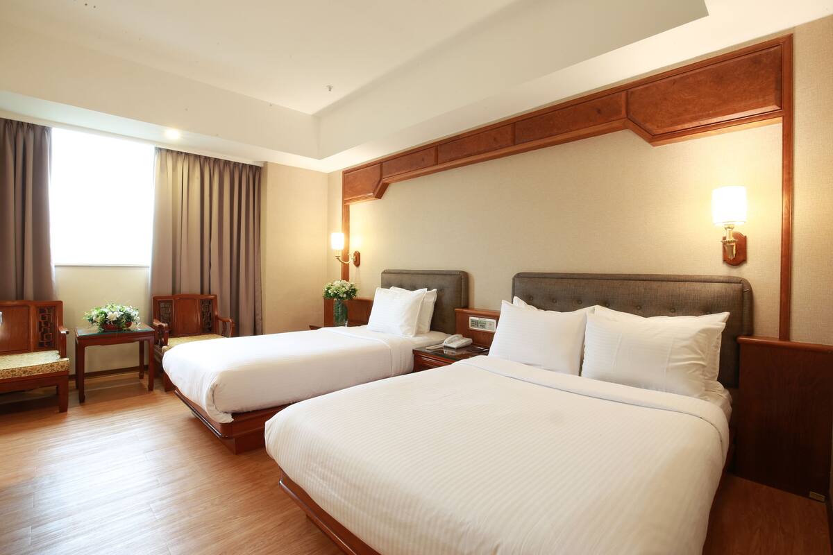 A hotel room with two beds, wooden headboards, a desk, and a chair.