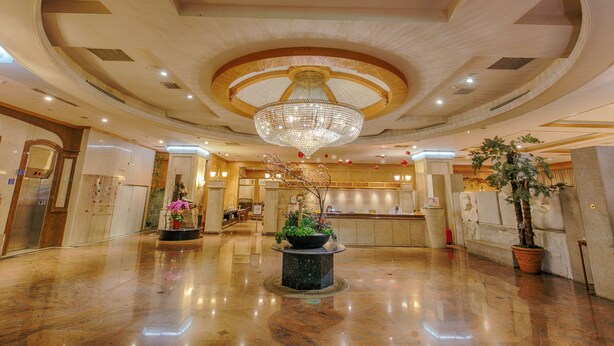 A spacious lobby with a grand chandelier, a reception desk, and a large potted plant.