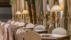 A banquet hall with rows of tables and chairs, draped curtains, and a large artificial tree.