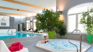 Een zwembadgedeelte van een hotel met een whirlpool, ligbedden en potplanten.