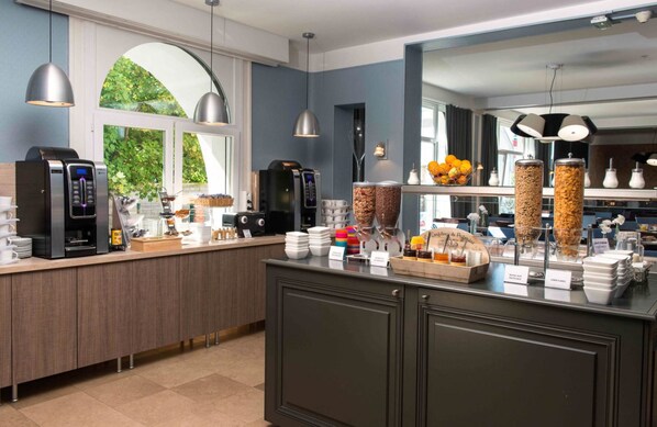 A modern kitchen with a coffee station, a fruit display, and a view of the outdoors. - Hôtel Régina (Berck-sur-Mer)