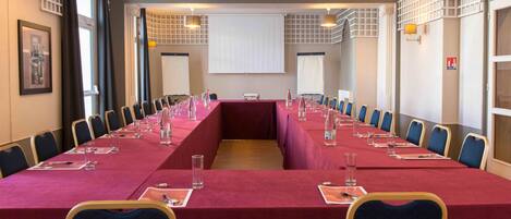 A conference room with a long table, chairs, and a projector screen.