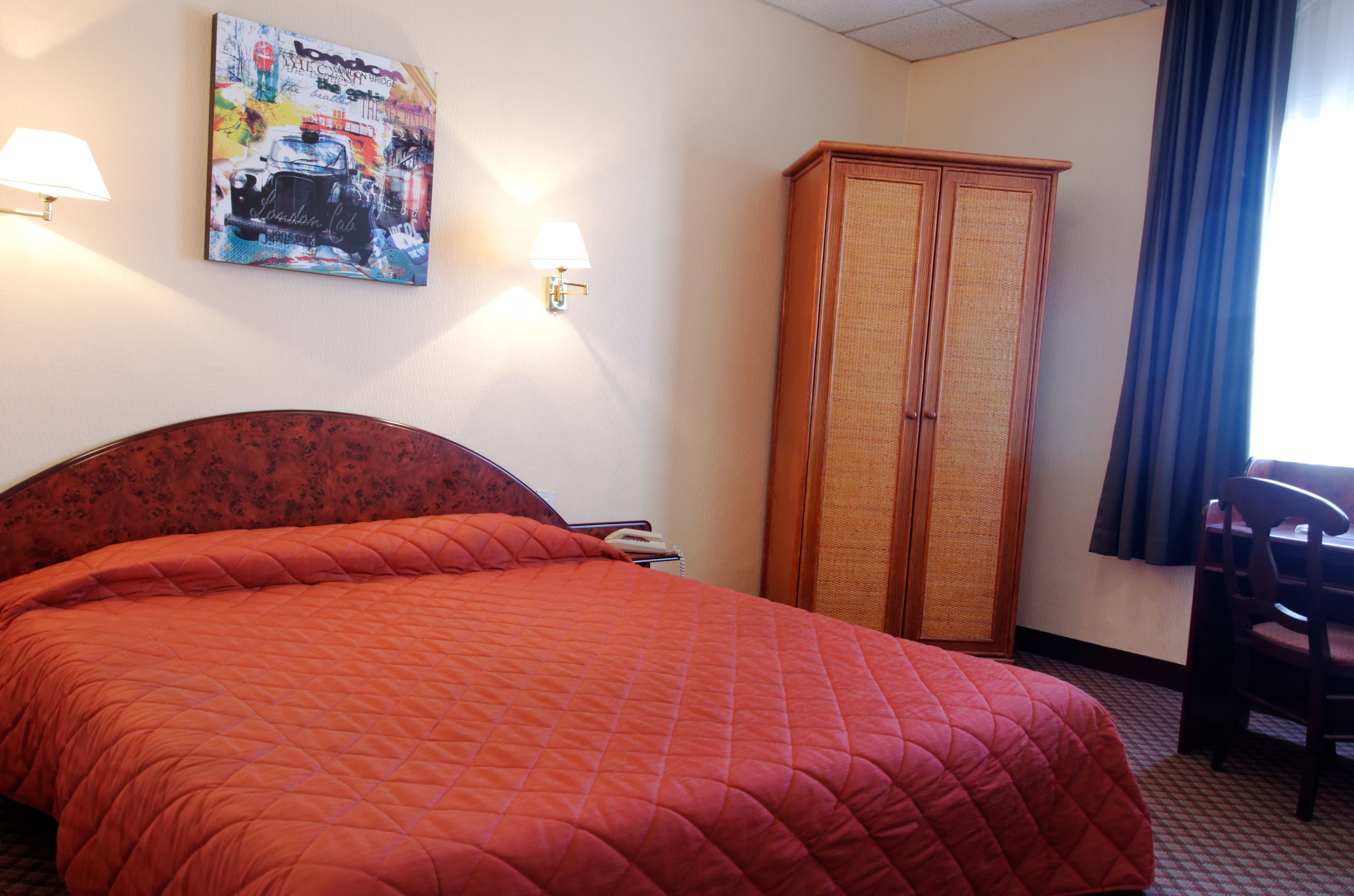 Ein Hotelzimmer mit einem großen Bett, einem Kleiderschrank, einem Schreibtisch und einer Lampe.