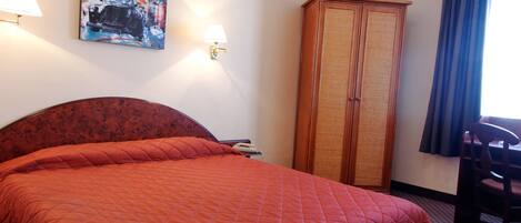 A hotel room with a large bed, a wardrobe, a desk, and a lamp.