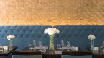 Un restaurante con pared de madera, asientos con cojines azules y flores blancas en jarrones.