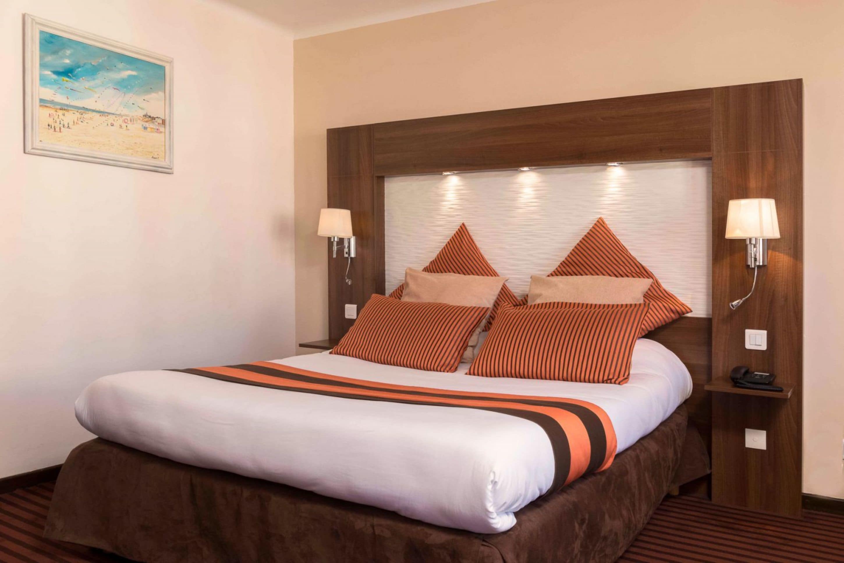 Una cama bien hecha con almohadillas a rayas, un cabecero de madera y dos lámparas de noche.