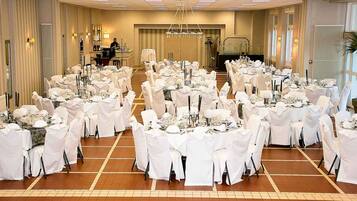 Een feestzaal met ronde tafels gedekt voor een formeel evenement, met witte tafellakens en stoelen, en een kroonluchter in het midden.