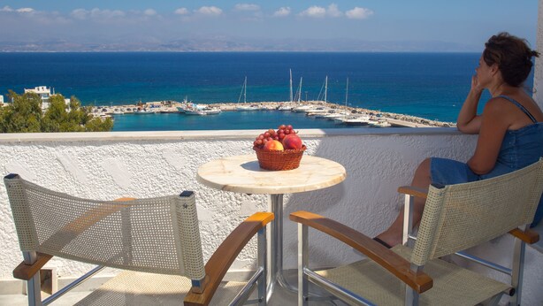 A balcony with a table and chairs overlooking a marina with boats and a clear blue sea. - Arkas Inn (Paros)