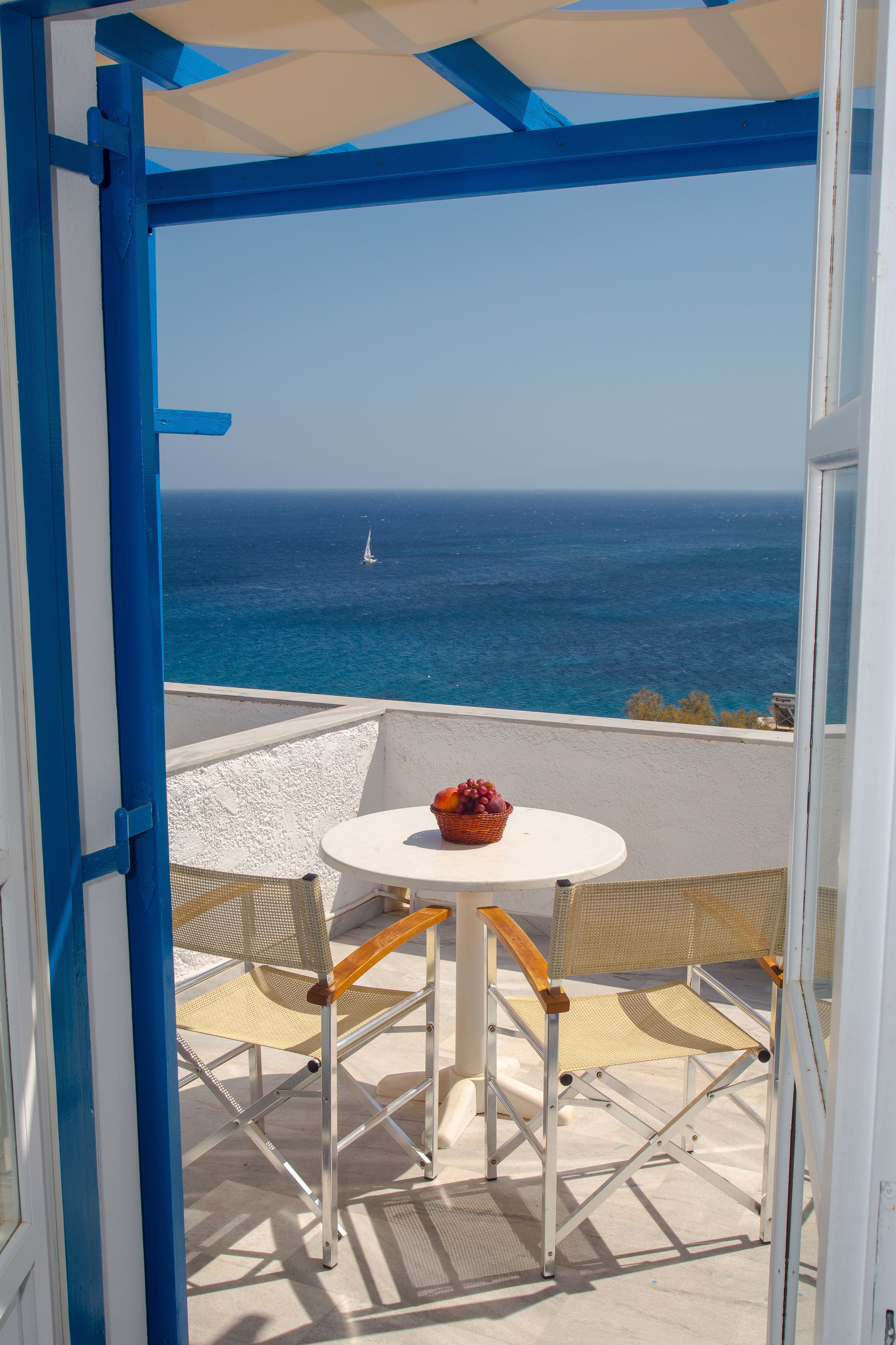 Un balcon avec une table blanche et deux chaises en osier, donnant sur la mer.