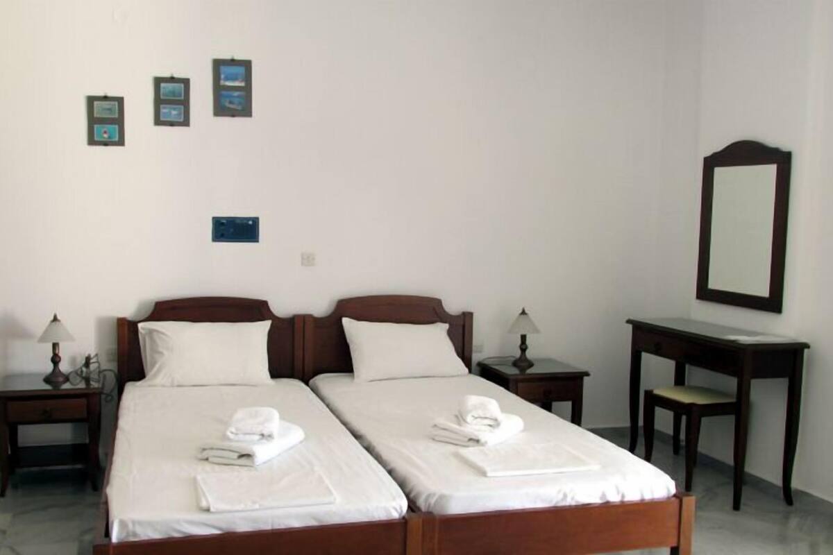 A hotel room with two beds, a desk, a chair, a mirror, and three framed pictures on the wall.