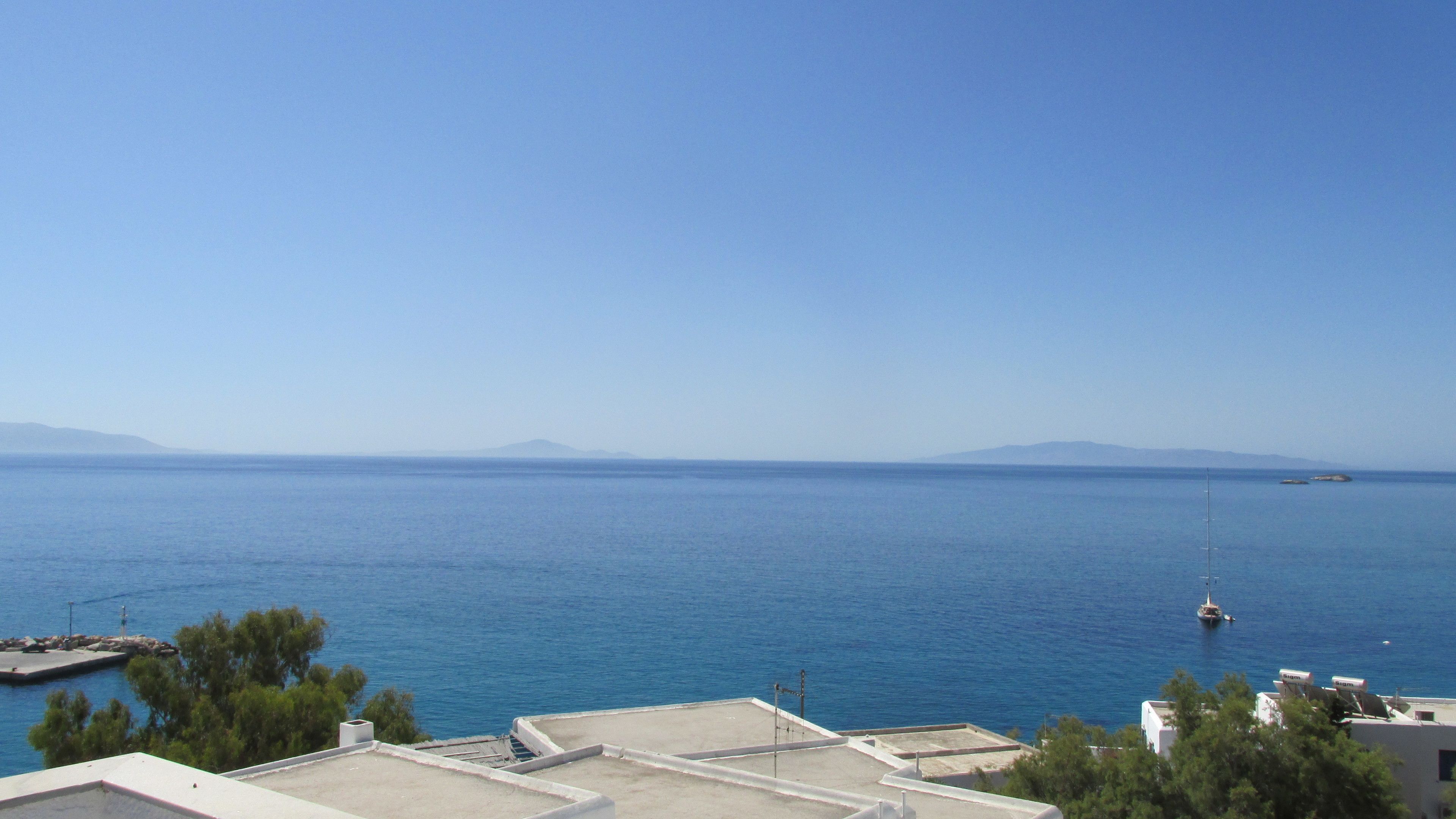 Une vue sur la côte, avec un ciel dégagé, une mer calme et des montagnes à l’horizon.