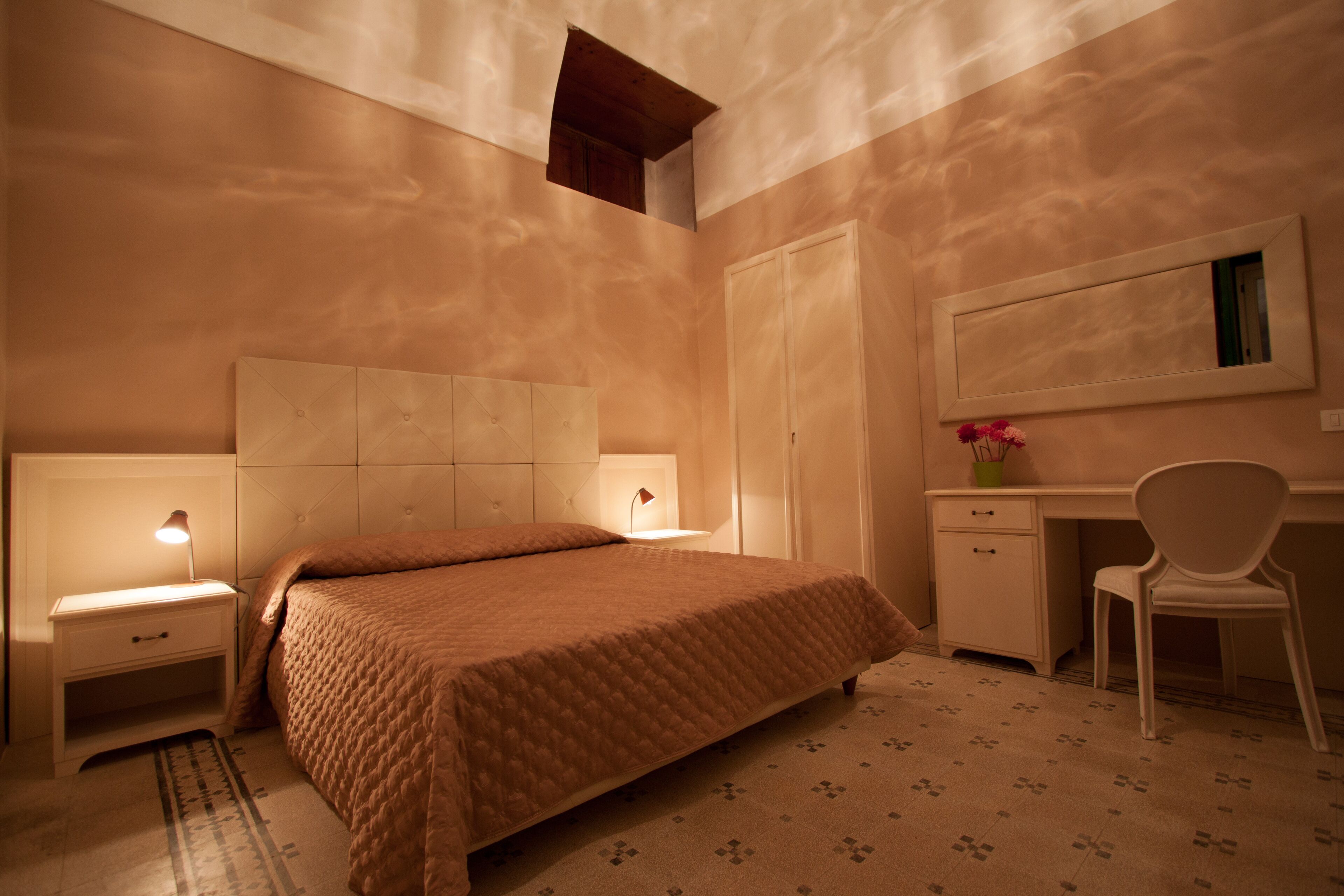 Ein Schlafzimmer mit Bett, Nachttisch, Schreibtisch, Stuhl und einem kleinen Fenster.