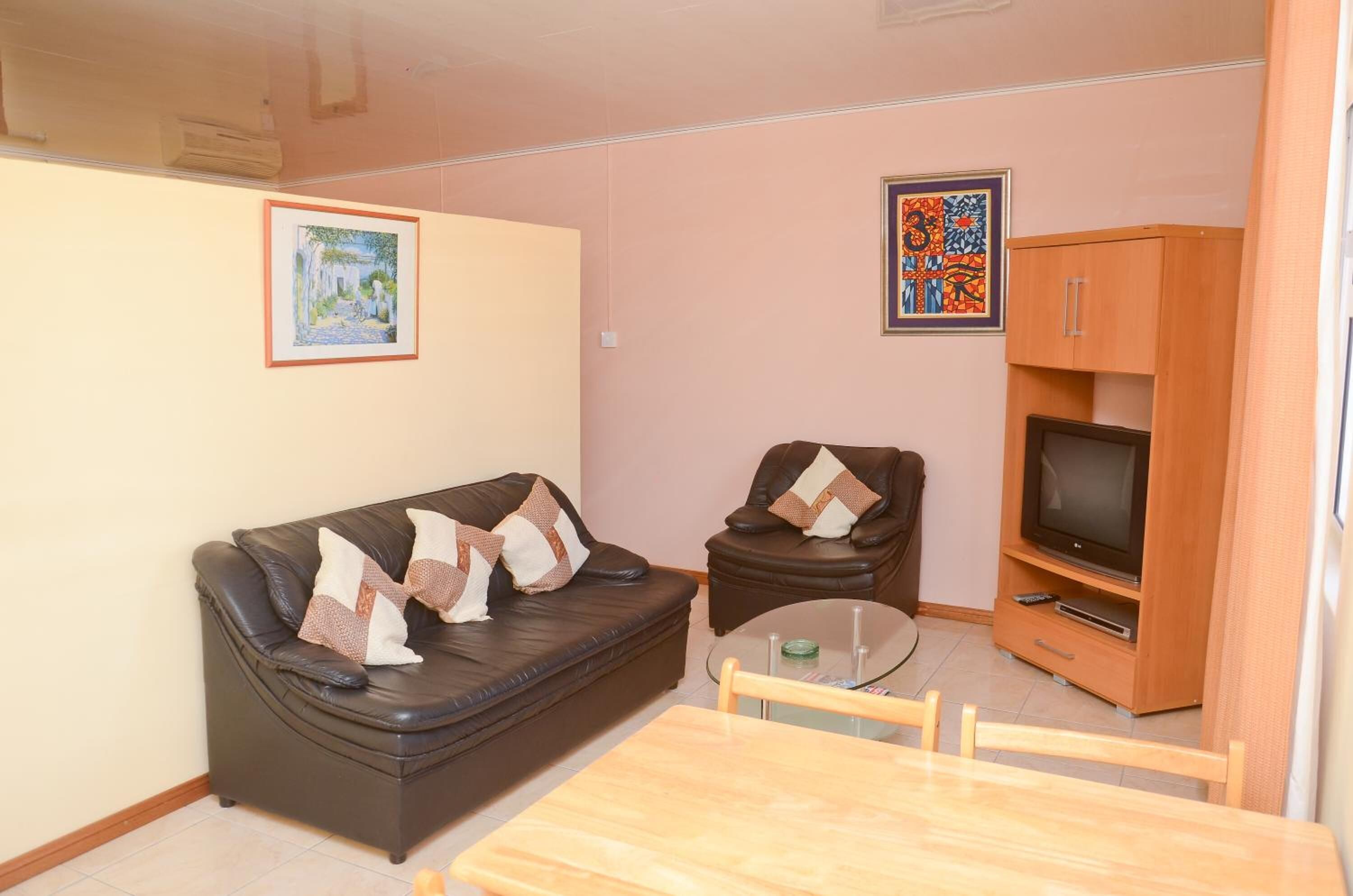 Una sala de estar con sofá, sillón, mueble para televisión y una mesita.