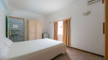 Ein Hotelzimmer mit Bett, kleinem Badezimmer mit Waschbecken, Kleiderschrank und einem Fenster mit Vorhängen.
