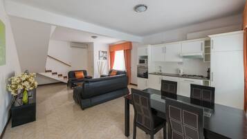 A modern apartment with a living room, dining area, and kitchen. There is a staircase leading to an upper level.