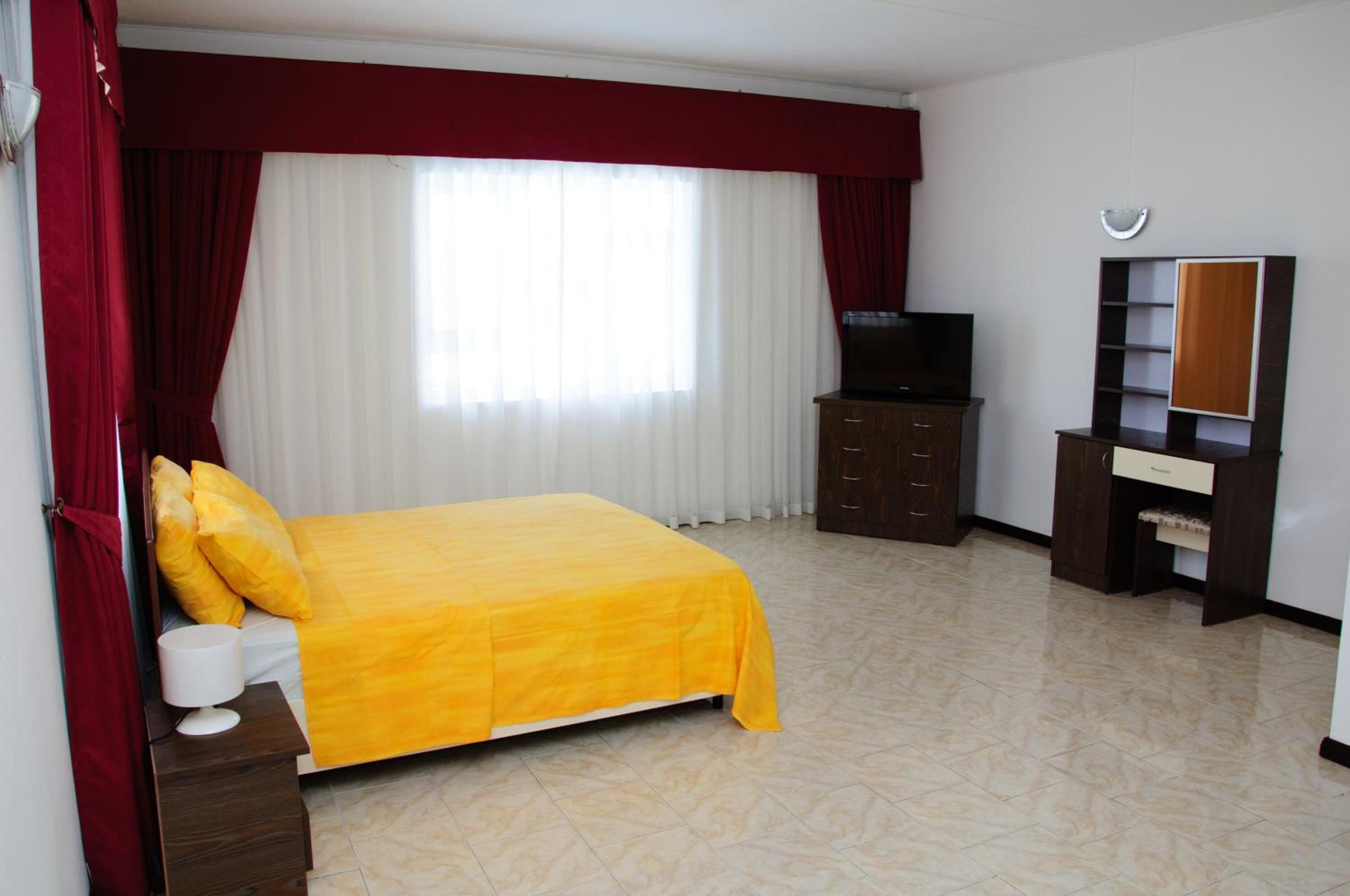 A hotel room with a bed, a TV, a wardrobe, and a desk with a lamp.