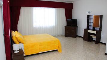 A hotel room with a bed, a TV, a wardrobe, and a desk with a lamp.
