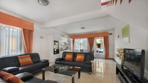 Uma sala de estar moderna com um sofá preto, uma mesa de centro de vidro e uma televisão de tela plana.