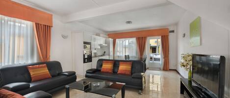 A modern living room with a black sofa set, a glass coffee table, and a flat-screen TV.