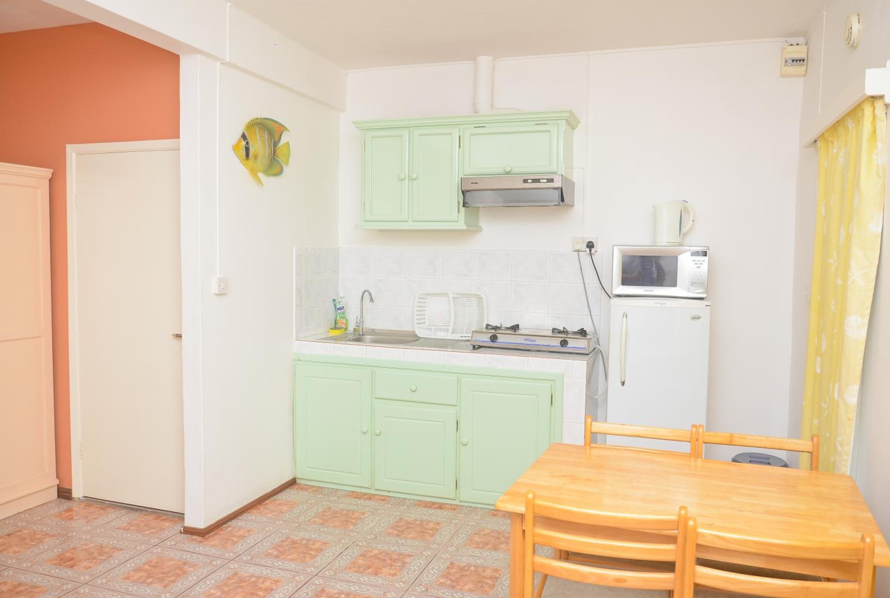 A compact kitchen with green cabinets, a microwave, a refrigerator, and a wooden dining table.