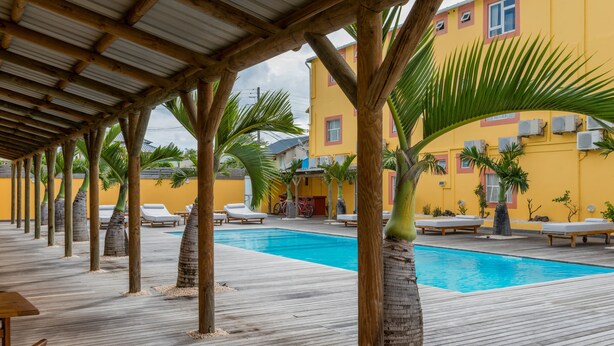Um deck de madeira com piscina, cadeiras de sol e palmeiras.