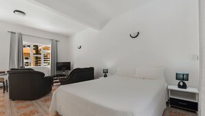 Quarto de hotel com uma cama grande, uma escrivaninha com computador, uma televisão e uma cadeira.