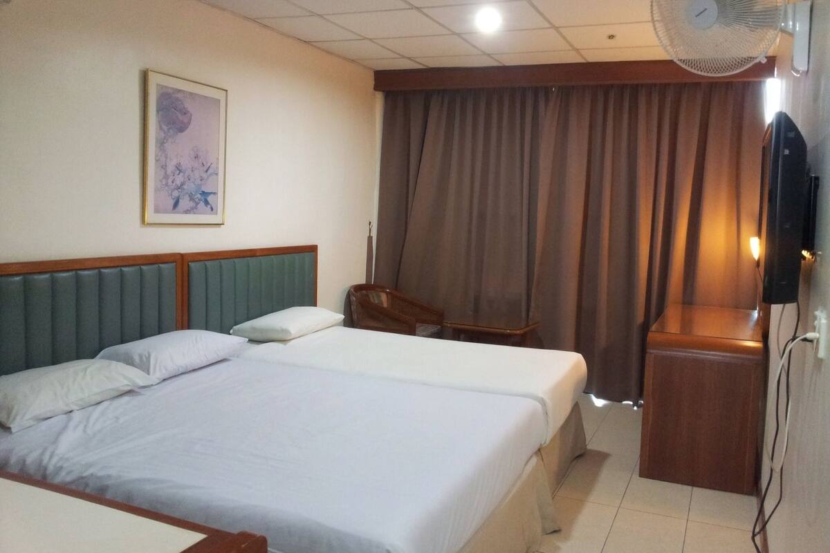 A hotel room with two beds, a ceiling fan, a television, and a window with curtains.