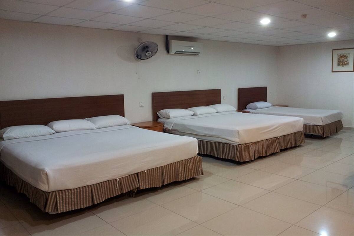 A hotel room with three single beds, each with a wooden headboard and white bedding.