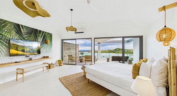 Un dormitorio moderno con una cama grande, televisión y balcón con vistas al mar.