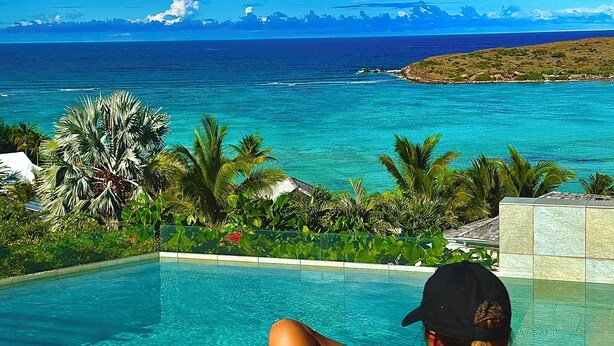 A person relaxing by a pool with a view of the ocean and mountains. - Amnios St Barth (St. Barthelemy)