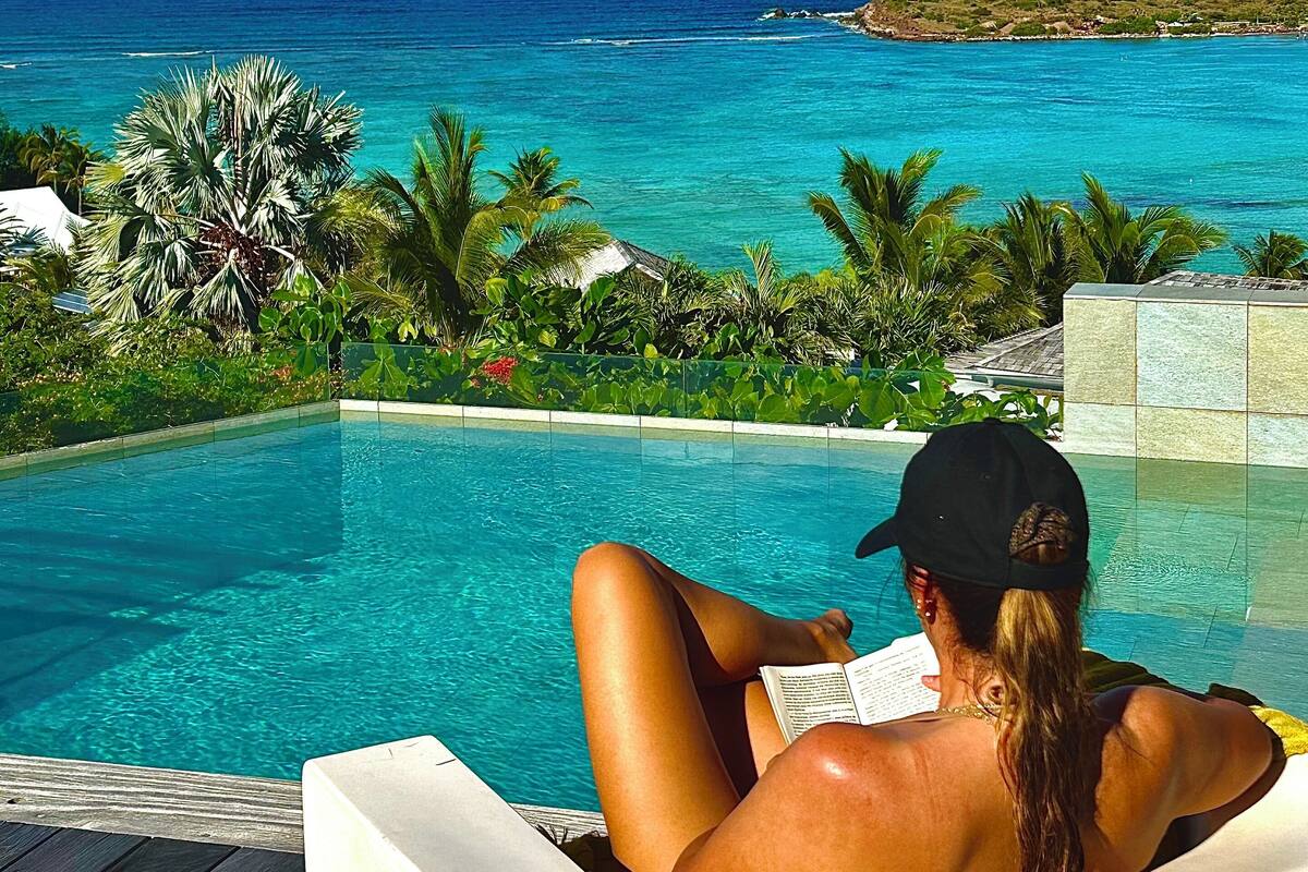 A person relaxing by a pool with a view of the ocean and mountains.
