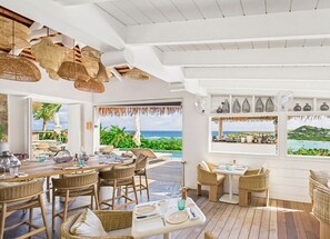 A restaurant with wicker furniture, a wooden deck, and a view of the ocean. - Amnios St Barth (St. Barthelemy)