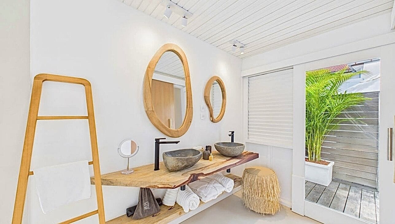 A modern bathroom with a wooden vanity, large mirrors, a sink, and a potted plant.