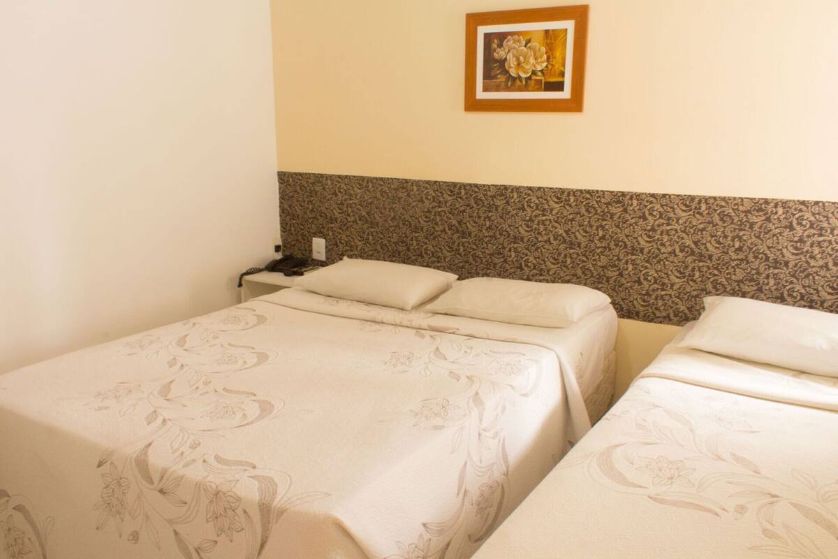 Quarto de hotel com duas camas, cabeceira estampada, mesa de cabeceira com telefone e quadro na parede.