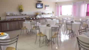 Un comedor con varias mesas y sillas, una zona de cocina con mostrador y electrodomésticos, y un televisor montado en la pared.