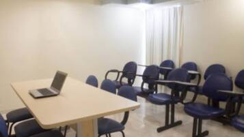 Une salle de conférence avec un ordinateur portable posé sur une table, plusieurs chaises et une fenêtre avec des rideaux.