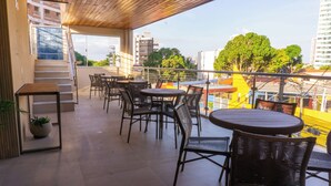 A covered outdoor seating area with wicker furniture and a view of the cityscape. - Hotel Água Marinha (Natal)