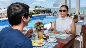Una mesa de comedor con vista al océano, una piscina y sombrillas.
