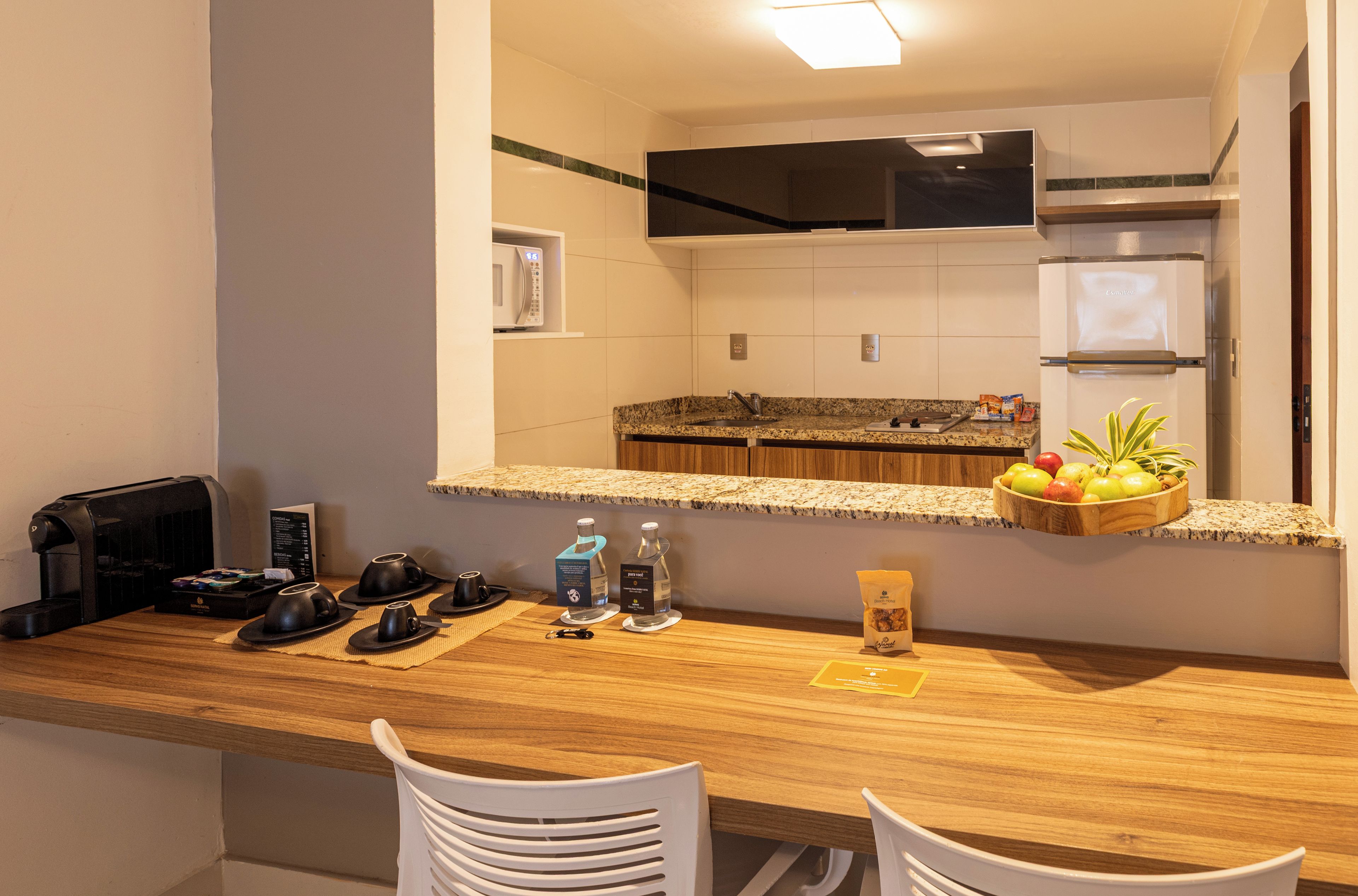 Une cuisine d’hôtel équipée d’un plan de travail en bois, d’un four à micro-ondes, d’une machine à café et d’un panier de fruits.