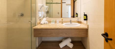 A bathroom with a glass shower enclosure, a wooden vanity with a sink, and a mirror.