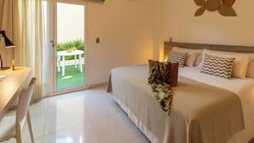 Quarto de hotel com cama, escrivaninha, cadeira e vista para um jardim através de uma porta deslizante.