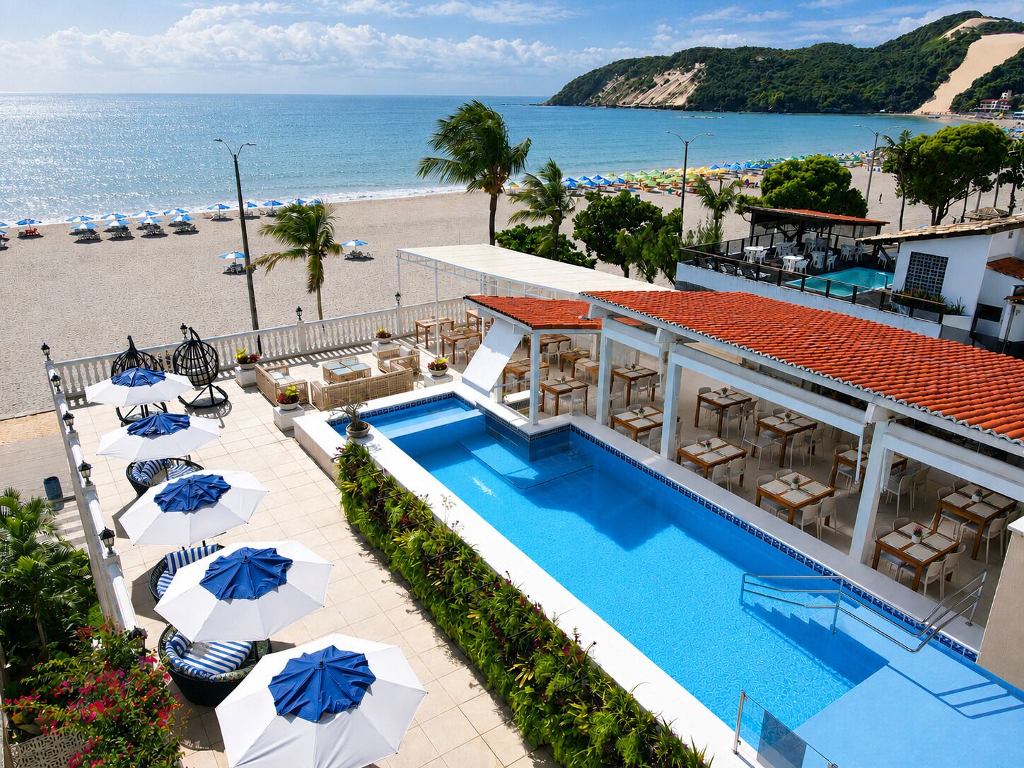 Área da piscina com vista para a praia, mobiliário de exterior e bar à beira da piscina.
