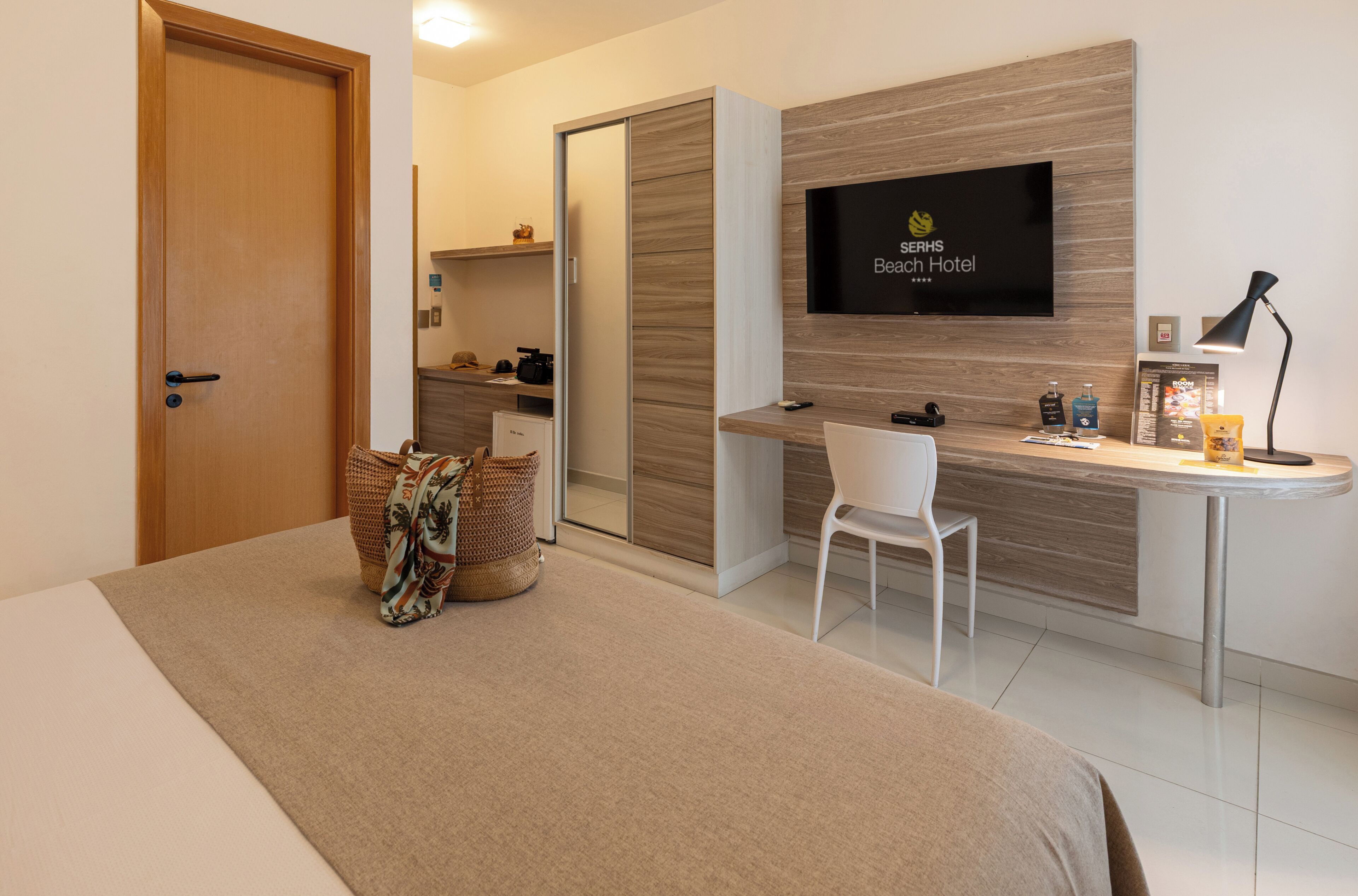 Habitación de hotel con cama, escritorio, silla, televisor y una pequeña cocina.