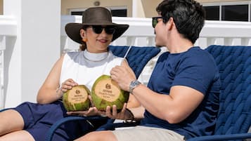 Dos personas sentadas en una silla de lounge azul al aire libre, sosteniendo dos cocos con el logo del SERHS Beach Hotel.