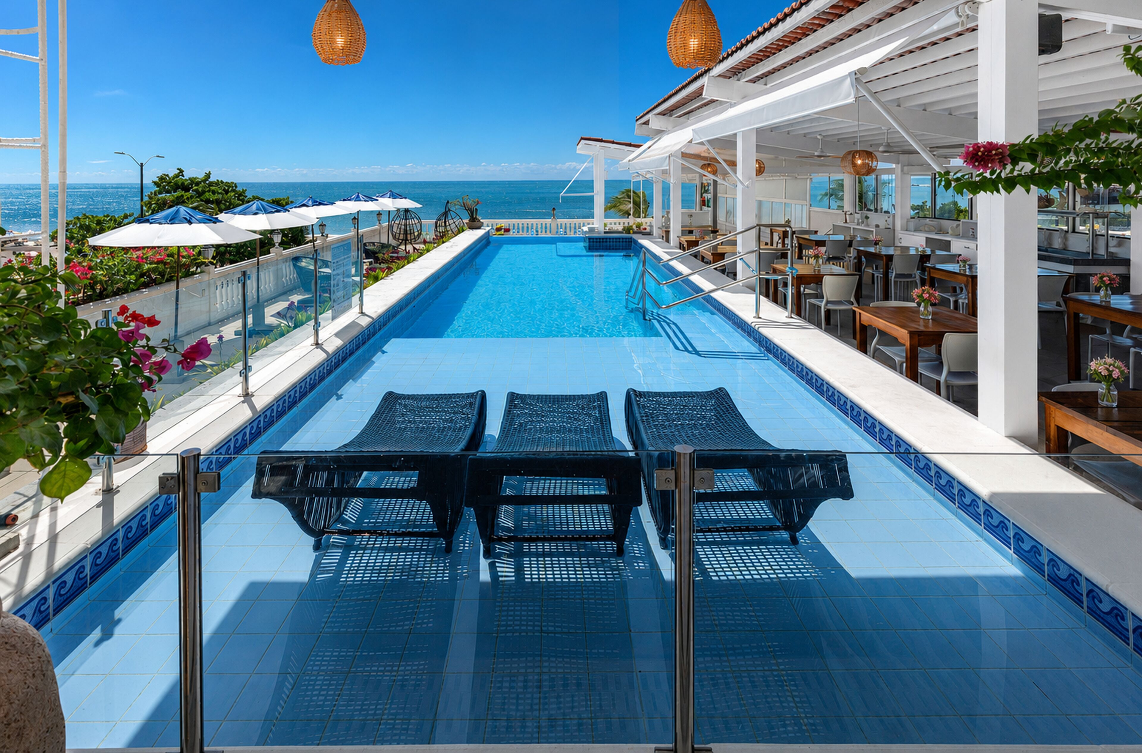 A pool area with lounge chairs, umbrellas, and a view of the ocean.