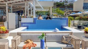 A pool area with a blue-tiled wall, wicker furniture, and a bar area with bottles and a plant.